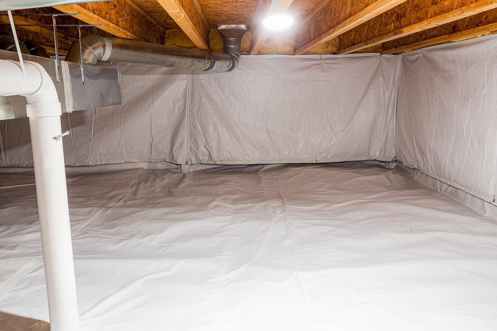 Crawl space fully encapsulated with thermoregulatory blankets and dimple board. Radon mitigation system pipes visible. Basement location for energy saving home improvement